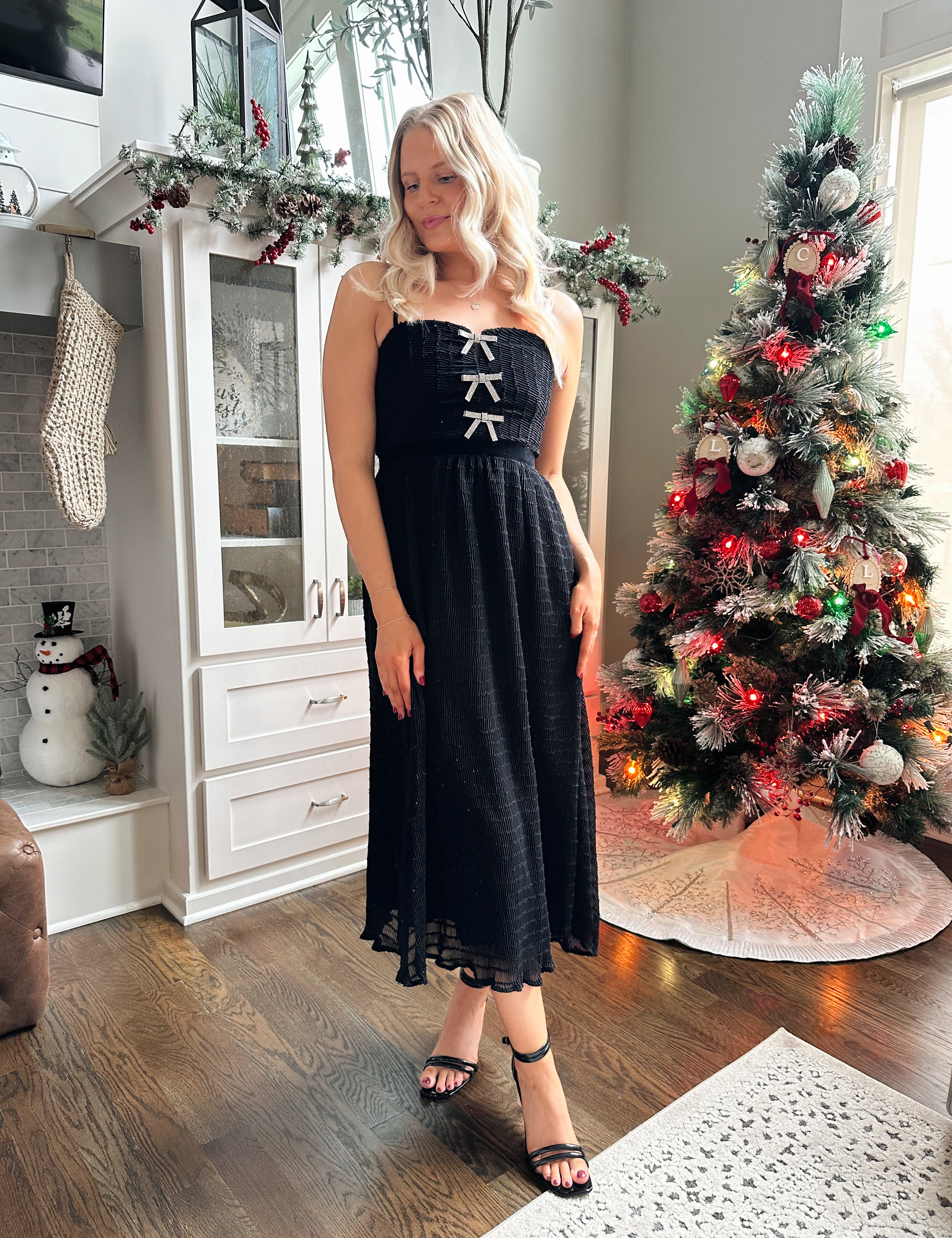Woman wearing black sparkle midi dress with rhinestone bow detailing. 