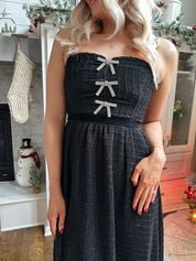 Woman wearing black sparkle midi dress with rhinestone bow detailing. 