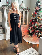 Woman wearing black sparkle midi dress with rhinestone bow detailing. 