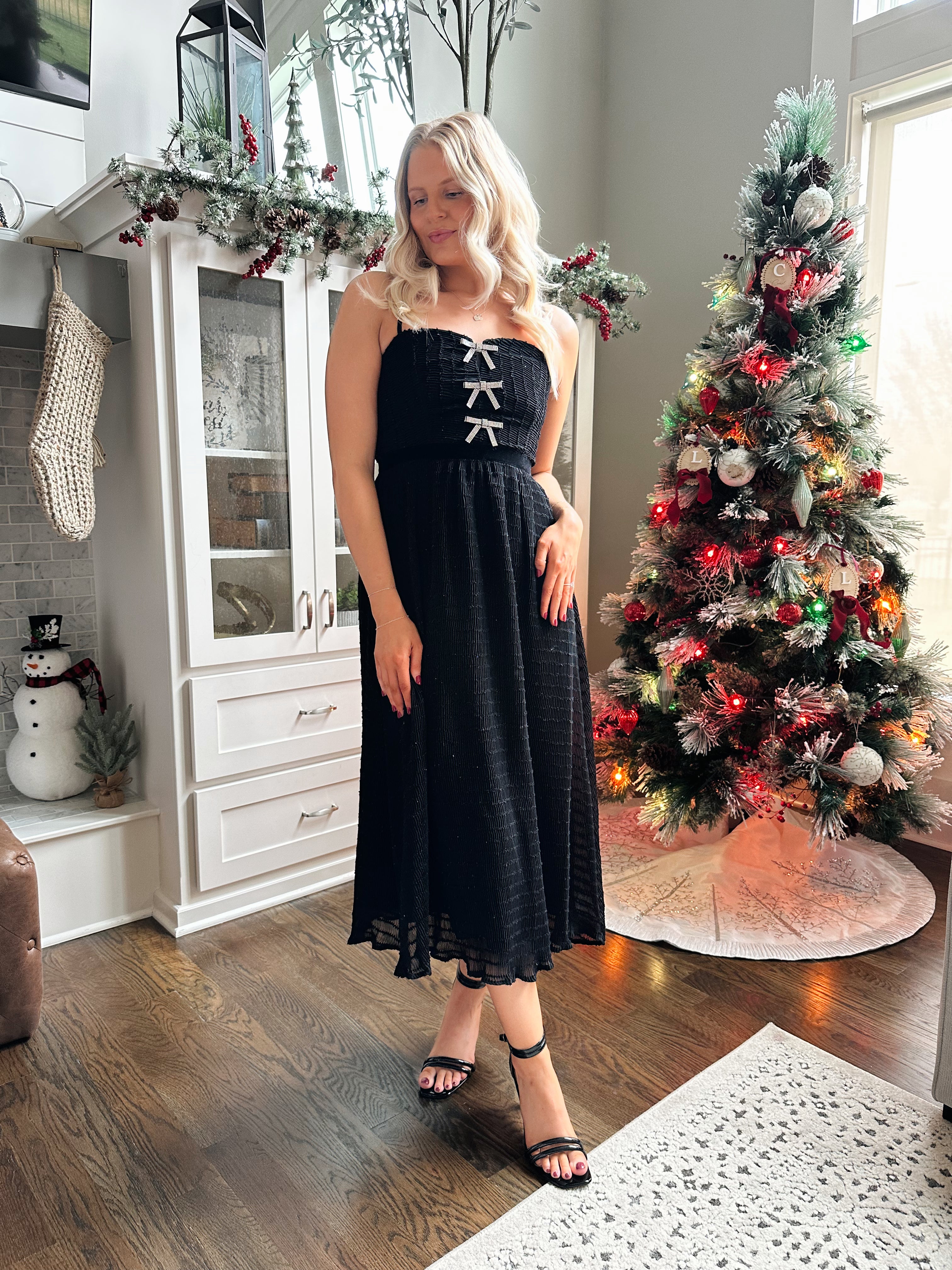 Woman wearing black sparkle midi dress with rhinestone bow detailing. 