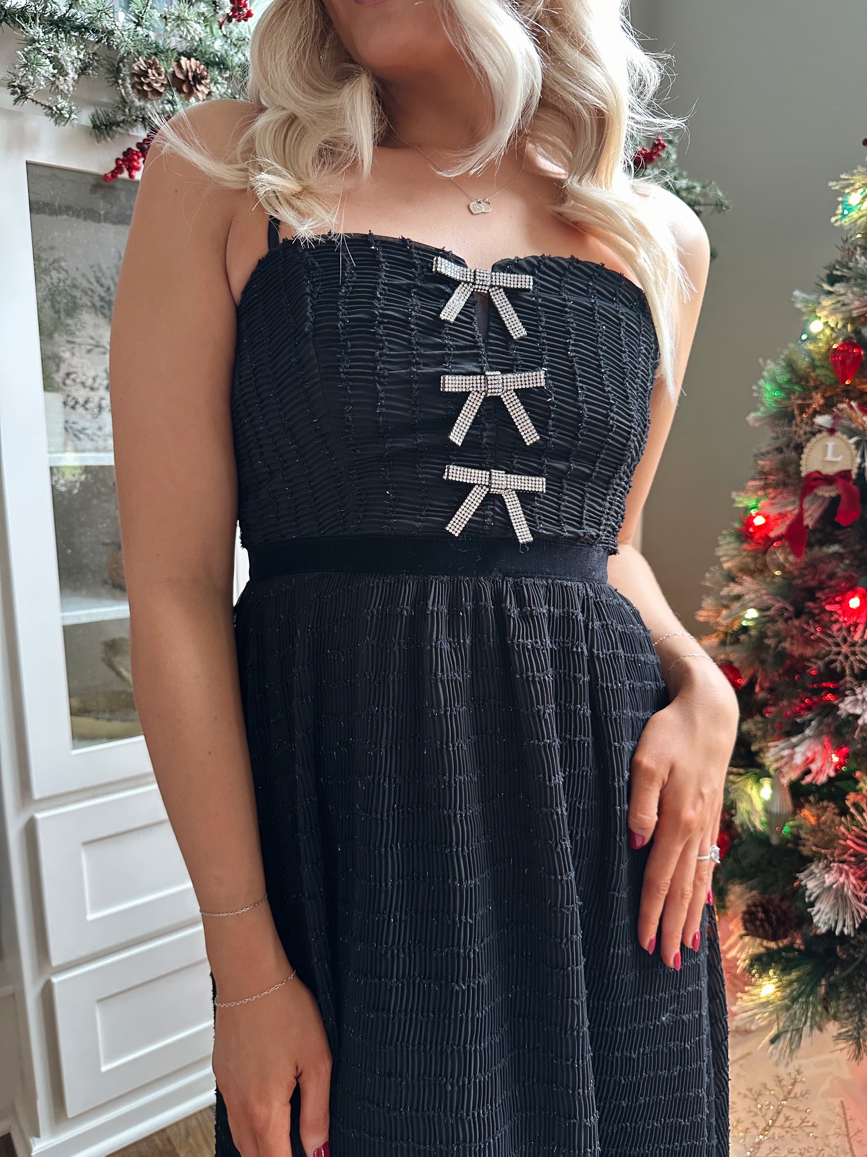 Woman wearing black sparkle midi dress with rhinestone bow detailing. 