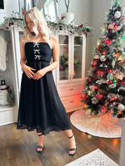 Woman wearing black sparkle midi dress with rhinestone bow detailing. 