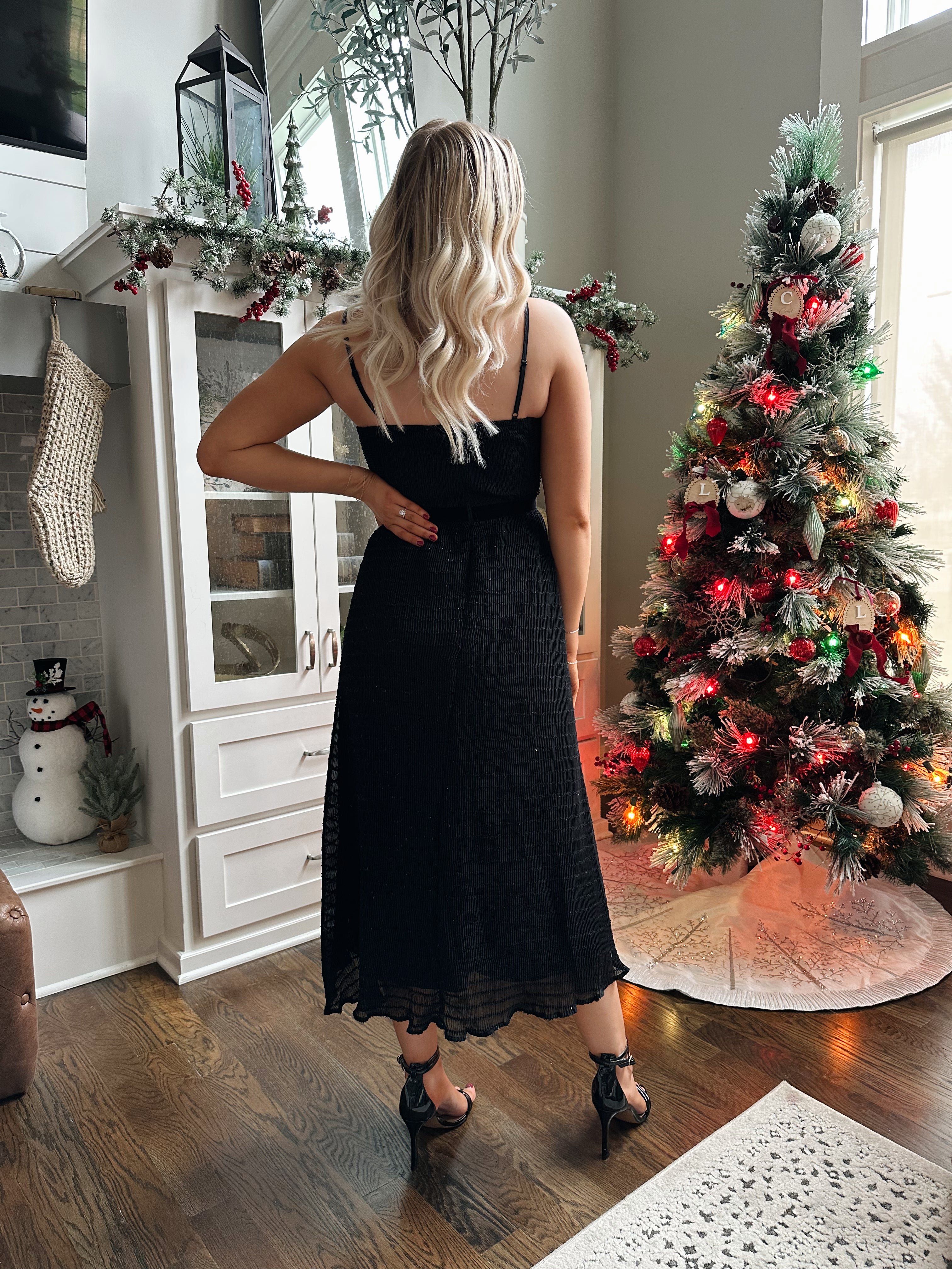 Woman wearing black sparkle midi dress with rhinestone bow detailing. 