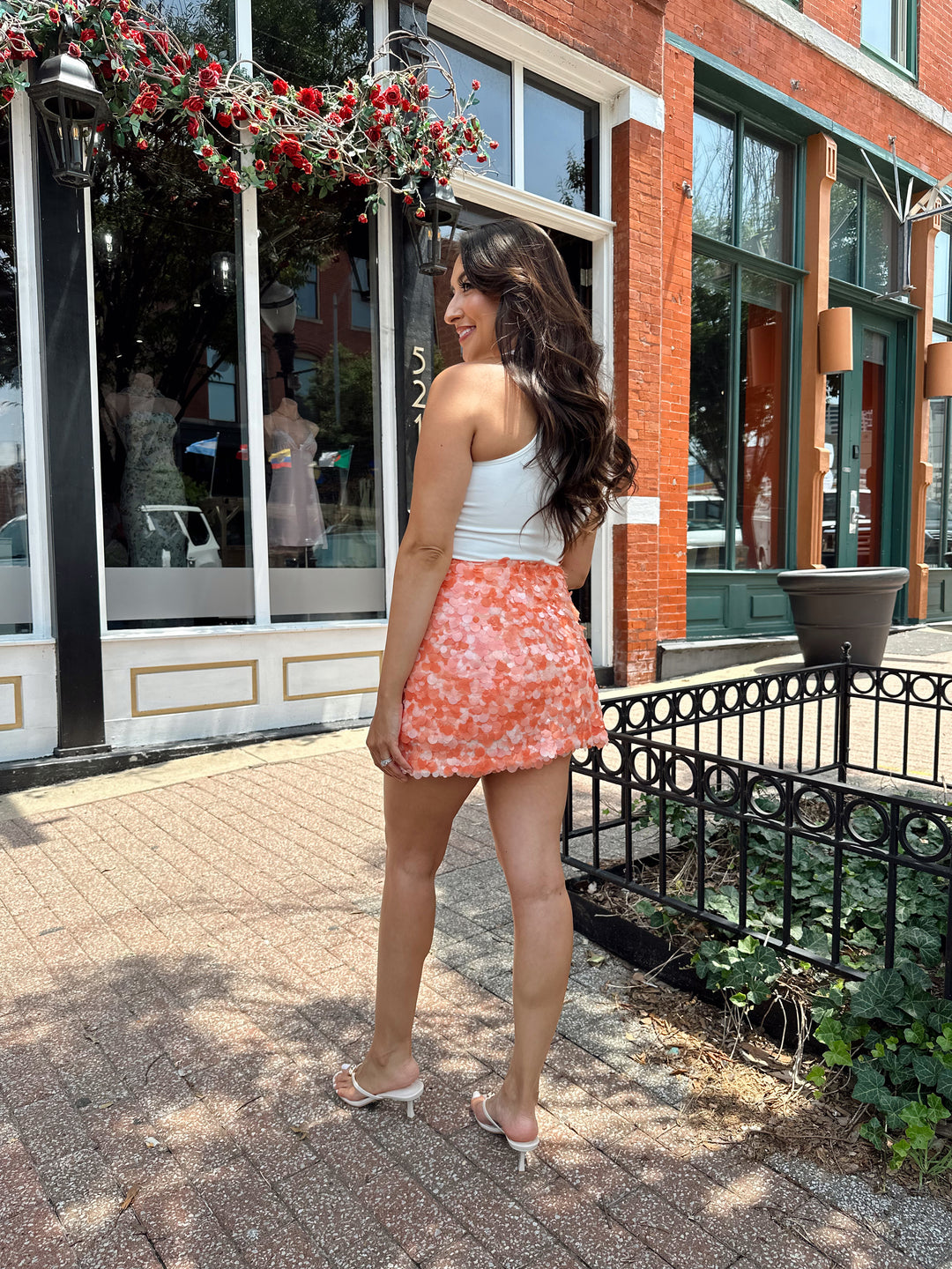Woman wearing white bodysuit with gold detail, and an orange sequin mini skirt. 