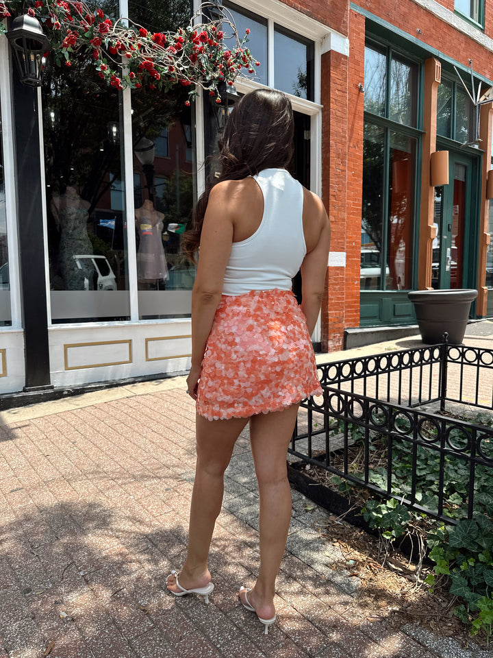 Woman wearing white bodysuit with gold detail, and an orange sequin mini skirt. 