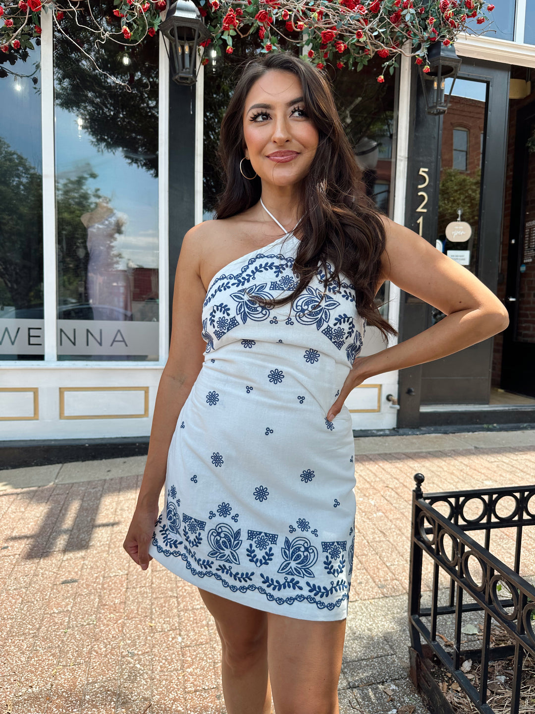 Woman wearing white halter mini dress with blue embroidery pattern.