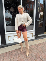Woman wearing cream chunky cardigan with gold button closure. 