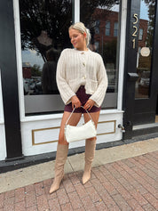 Woman wearing cream chunky cardigan with gold button closure. 