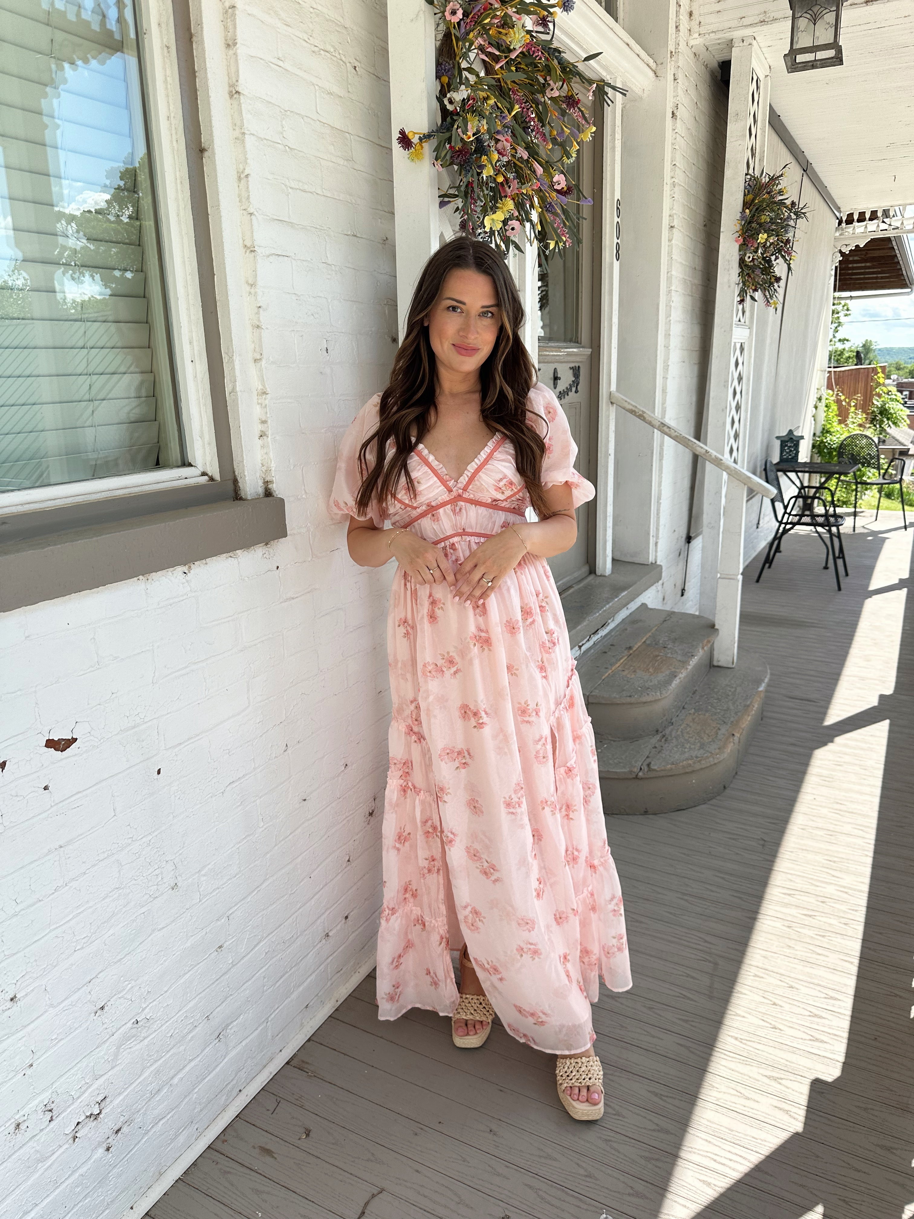 Woman in a pink floral maxi dress with puff sleeves, lace trim, and a subtle front slit
