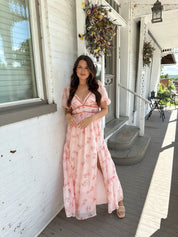 Woman in a pink floral maxi dress with puff sleeves, lace trim, and a subtle front slit