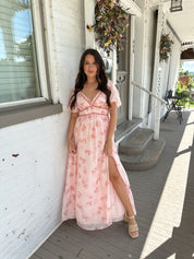 Woman in a pink floral maxi dress with puff sleeves, lace trim, and a subtle front slit