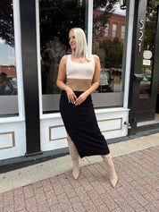 Woman wearing cream, beige and black ribbed midi dress with knee-high tan boots.