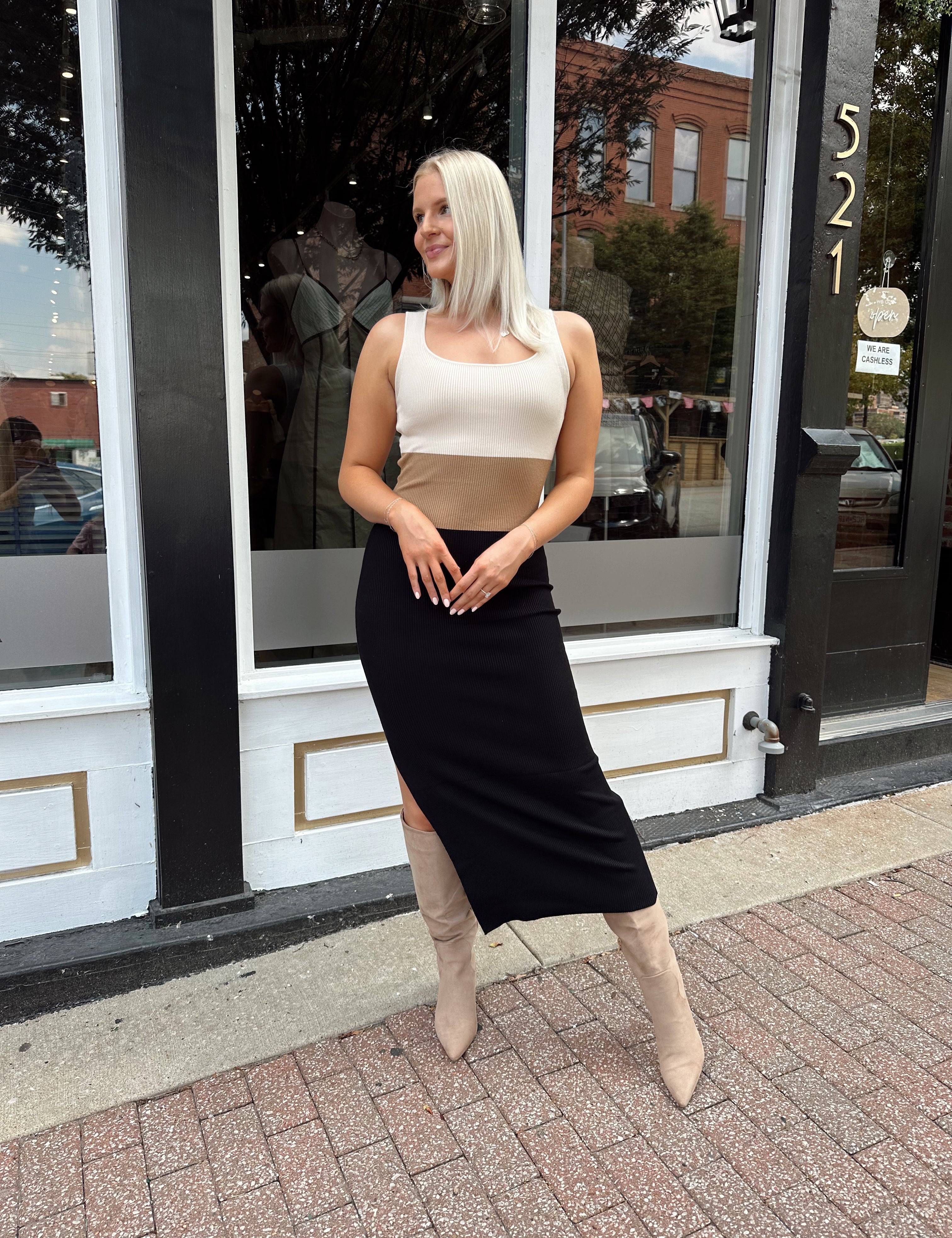 Woman wearing cream, beige and black ribbed midi dress with knee-high tan boots.