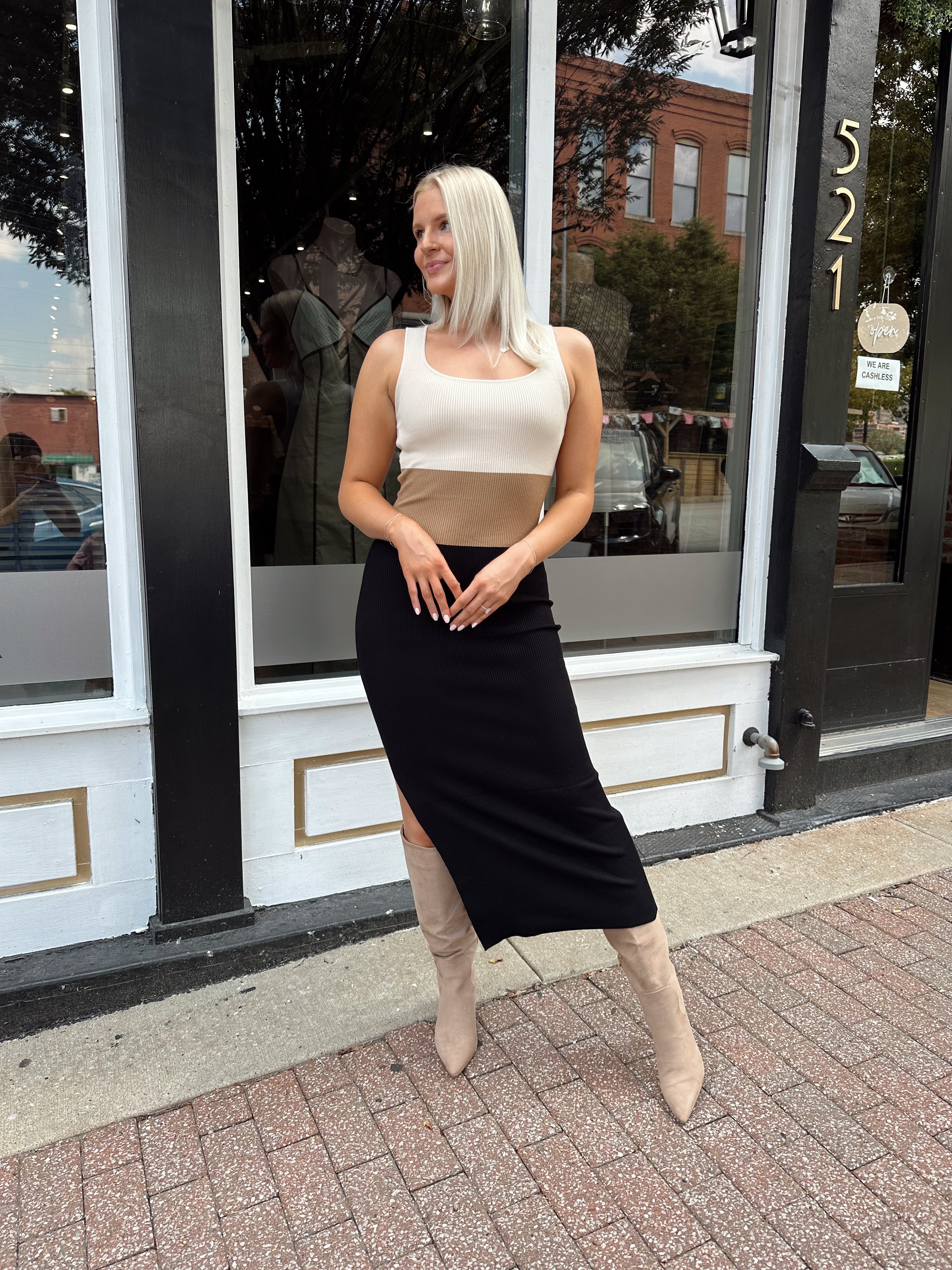 Woman wearing cream, beige and black ribbed midi dress with knee-high tan boots.