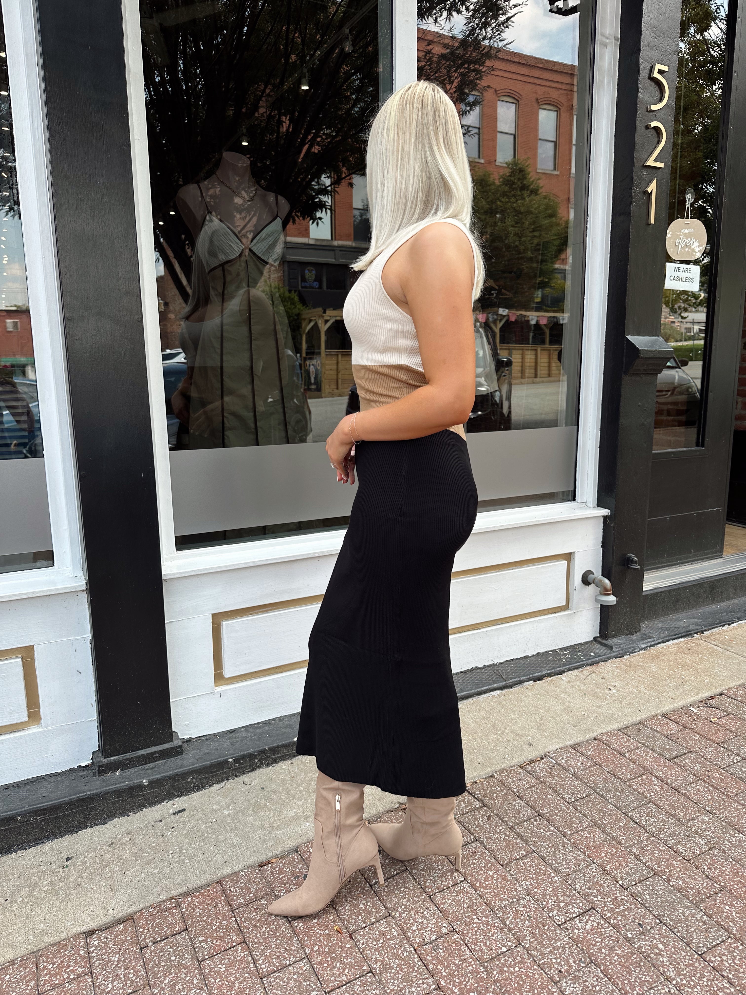 Woman wearing cream, beige and black ribbed midi dress with knee-high tan boots.