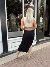 Woman wearing cream, beige and black ribbed midi dress with knee-high tan boots.