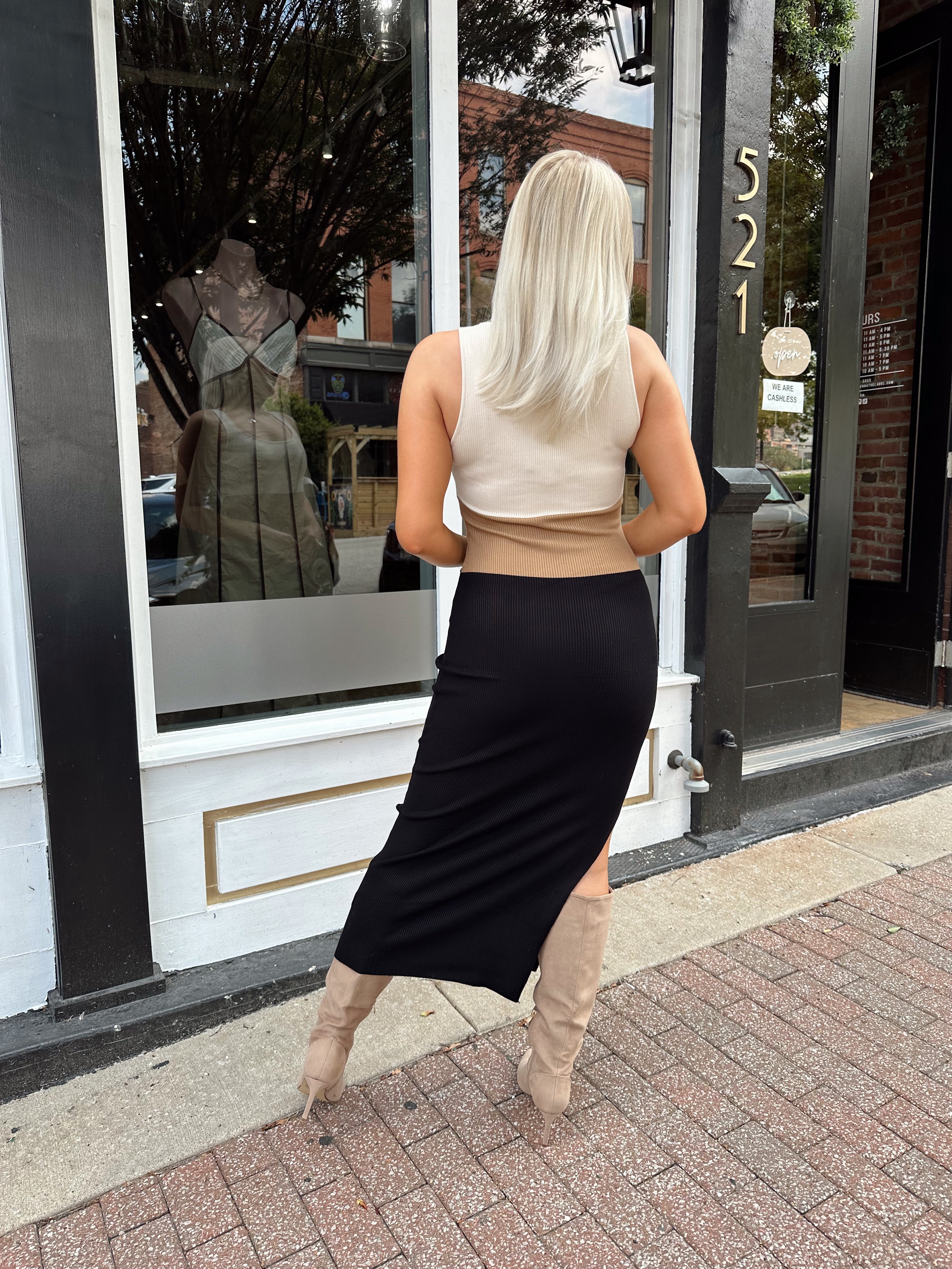 Woman wearing cream, beige and black ribbed midi dress with knee-high tan boots.