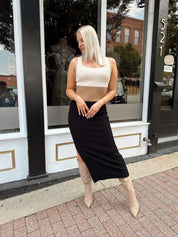 Woman wearing cream, beige and black ribbed midi dress with knee-high tan boots.