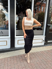 Woman wearing cream, beige and black ribbed midi dress with knee-high tan boots.