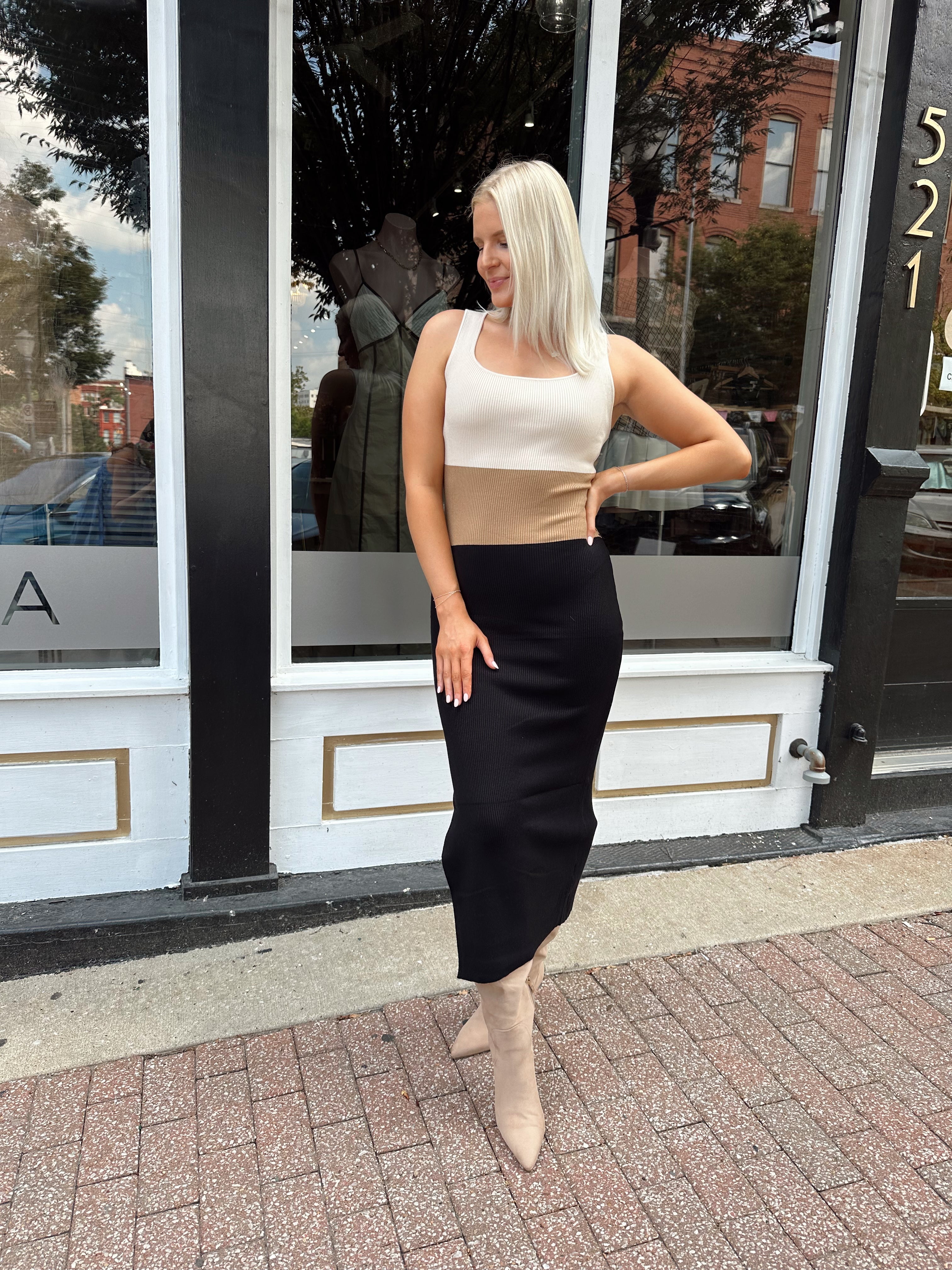 Woman wearing cream, beige and black ribbed midi dress with knee-high tan boots.