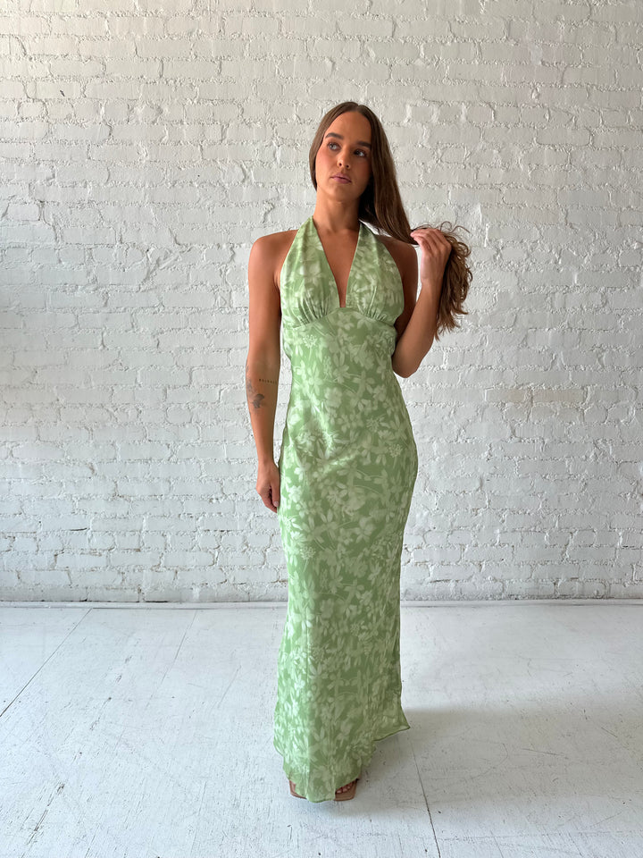 Woman wearing green floral halter maxi dress with open back and cowl detailing. 