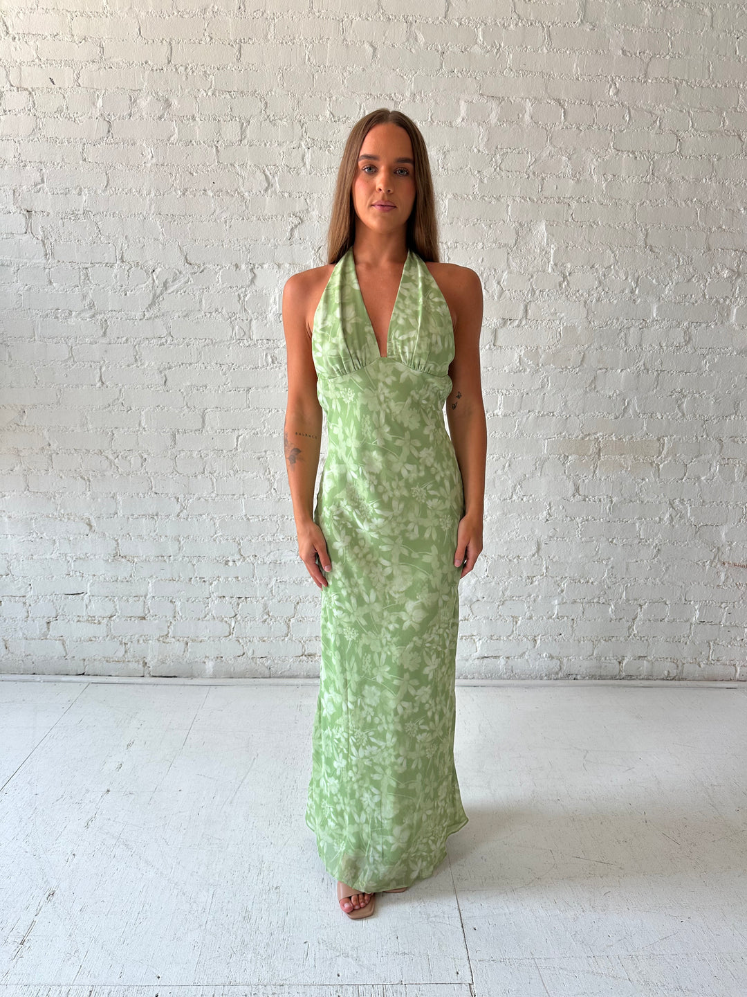 Woman wearing green floral halter maxi dress with open back and cowl detailing. 
