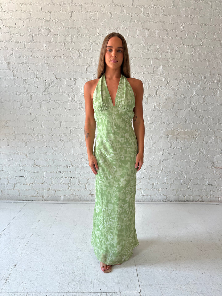 Woman wearing green floral halter maxi dress with open back and cowl detailing. 