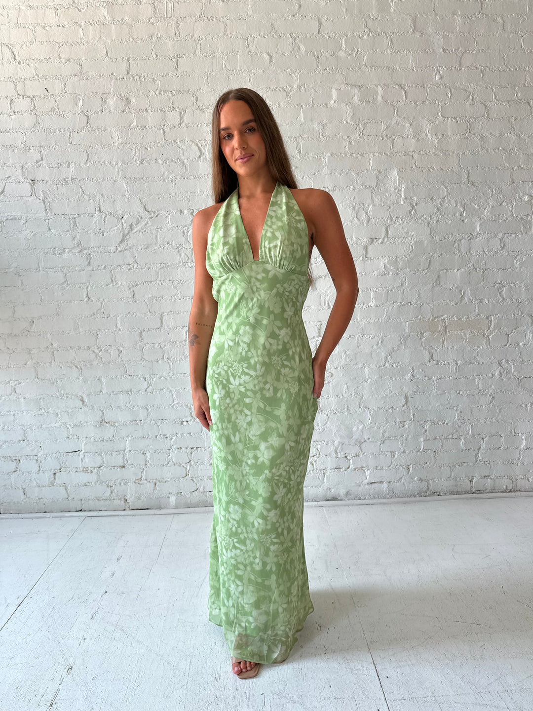 Woman wearing green floral halter maxi dress with open back and cowl detailing. 