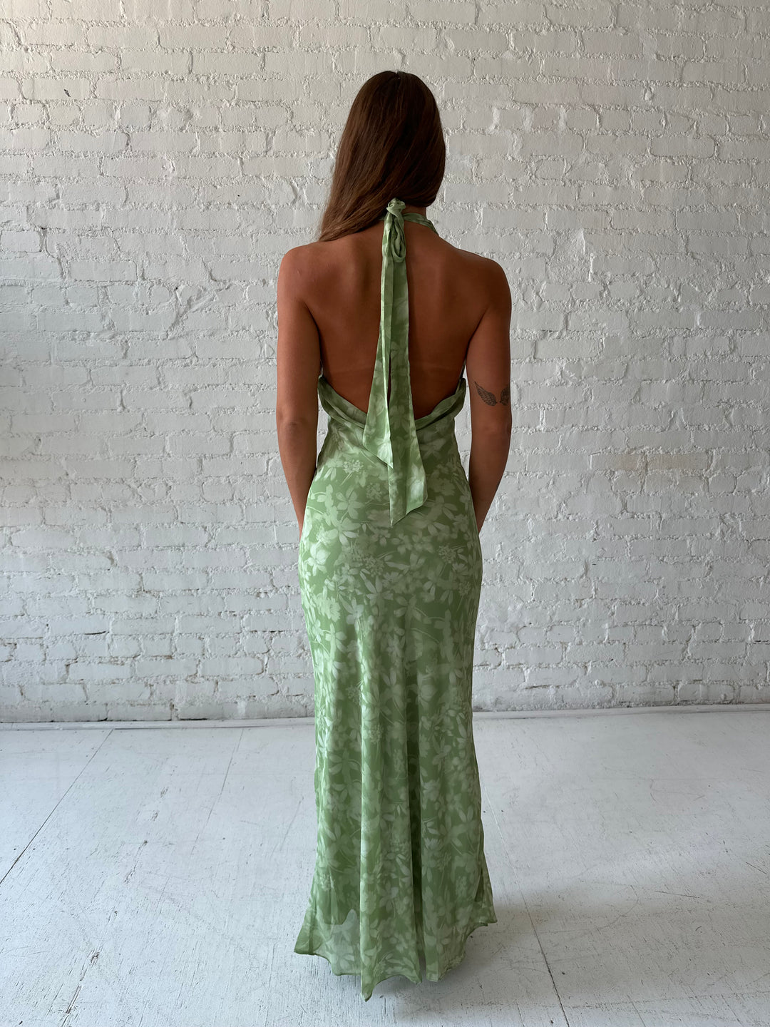 Woman wearing green floral halter maxi dress with open back and cowl detailing. 