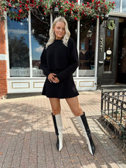 Woman wearing black sweater two piece set with long sleeve top and mini skirt. 