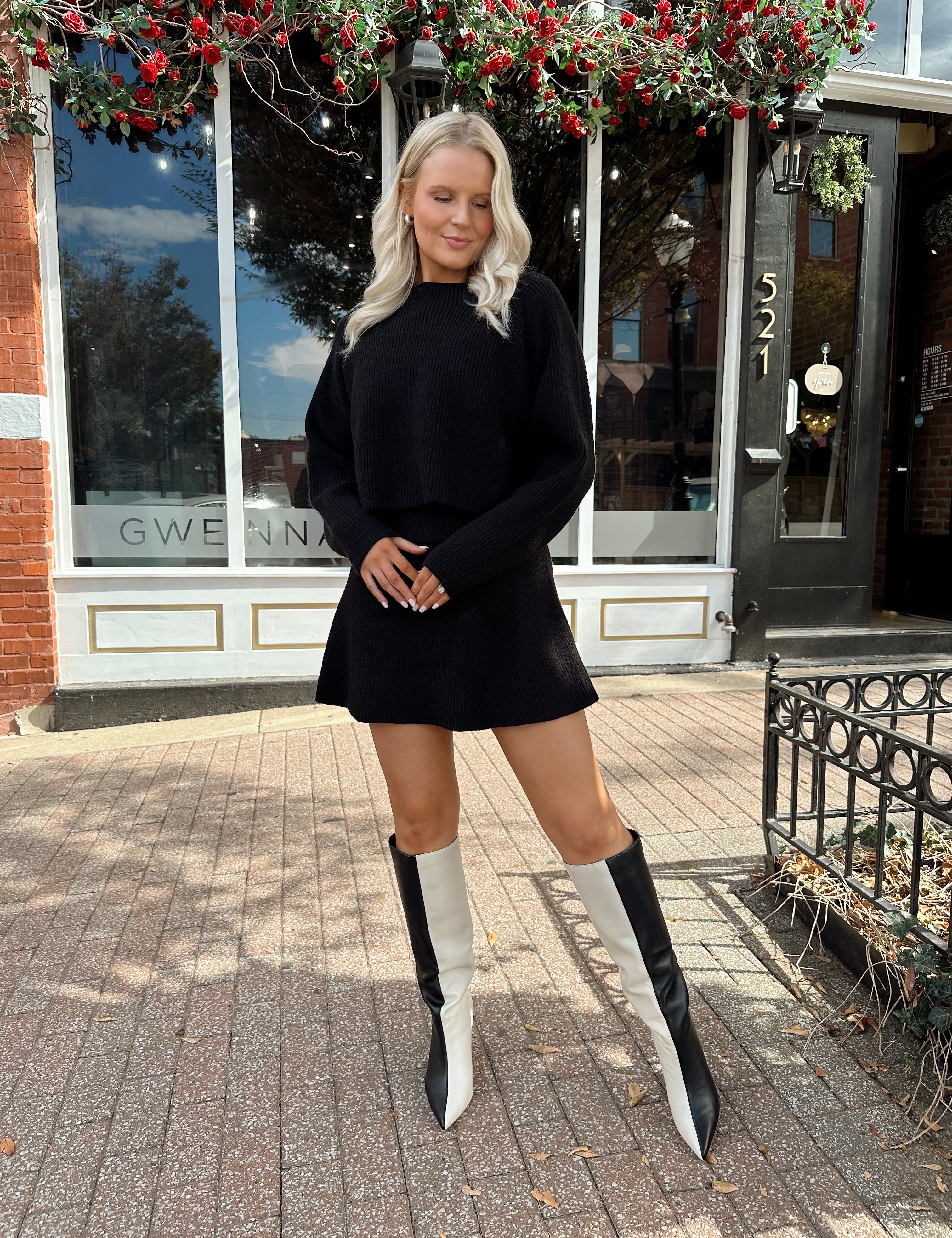Woman wearing black sweater two piece set with long sleeve top and mini skirt. 