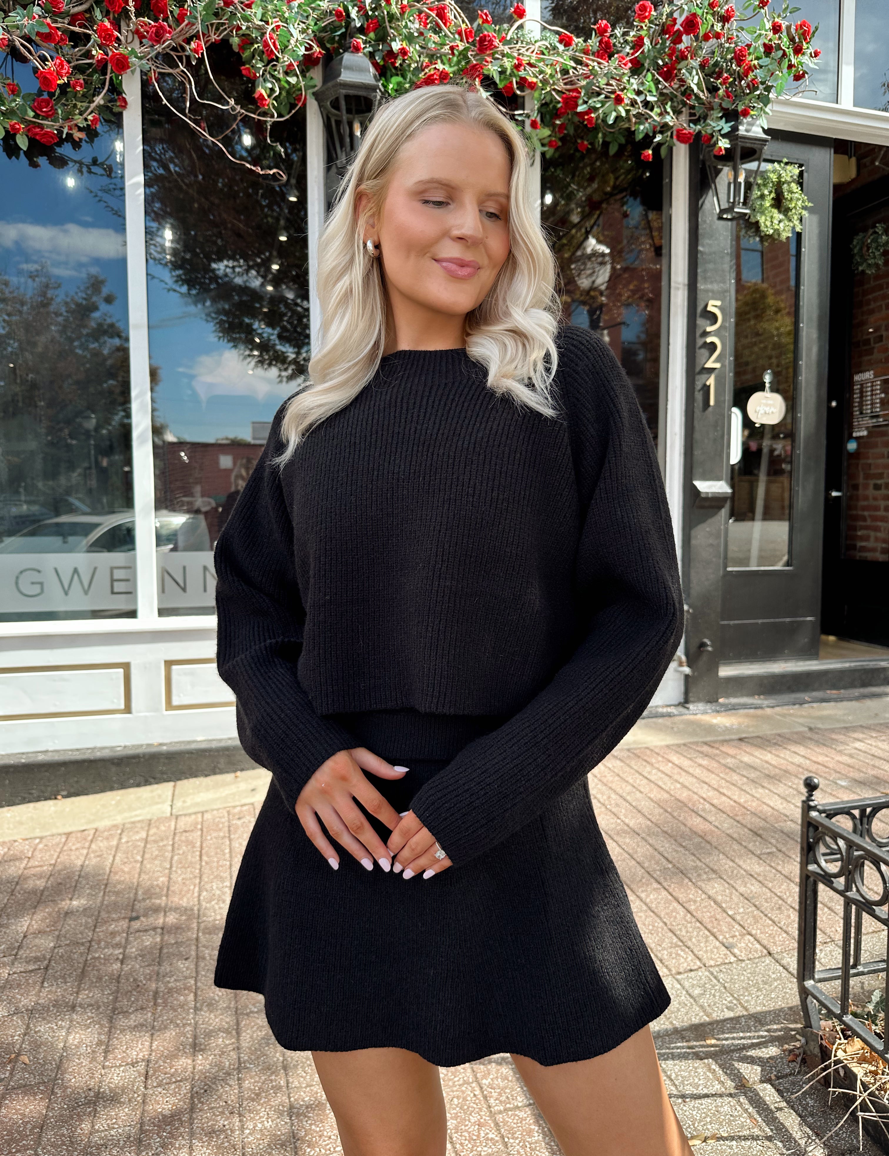 Woman wearing black sweater two piece set with long sleeve top and mini skirt. 
