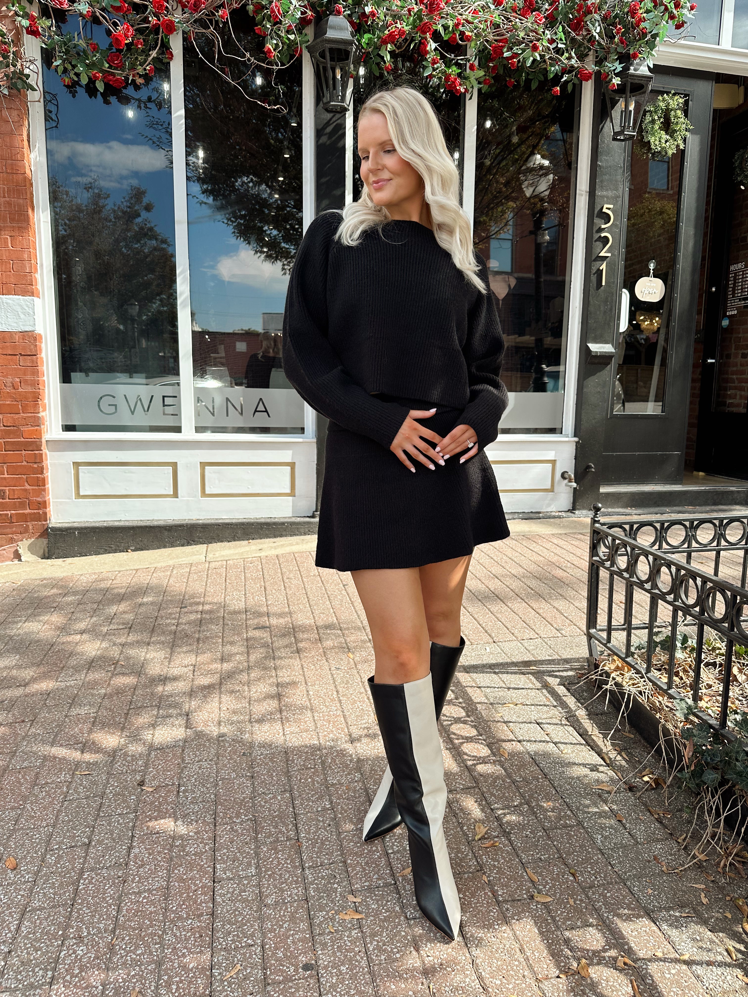 Woman wearing black sweater two piece set with long sleeve top and mini skirt. 