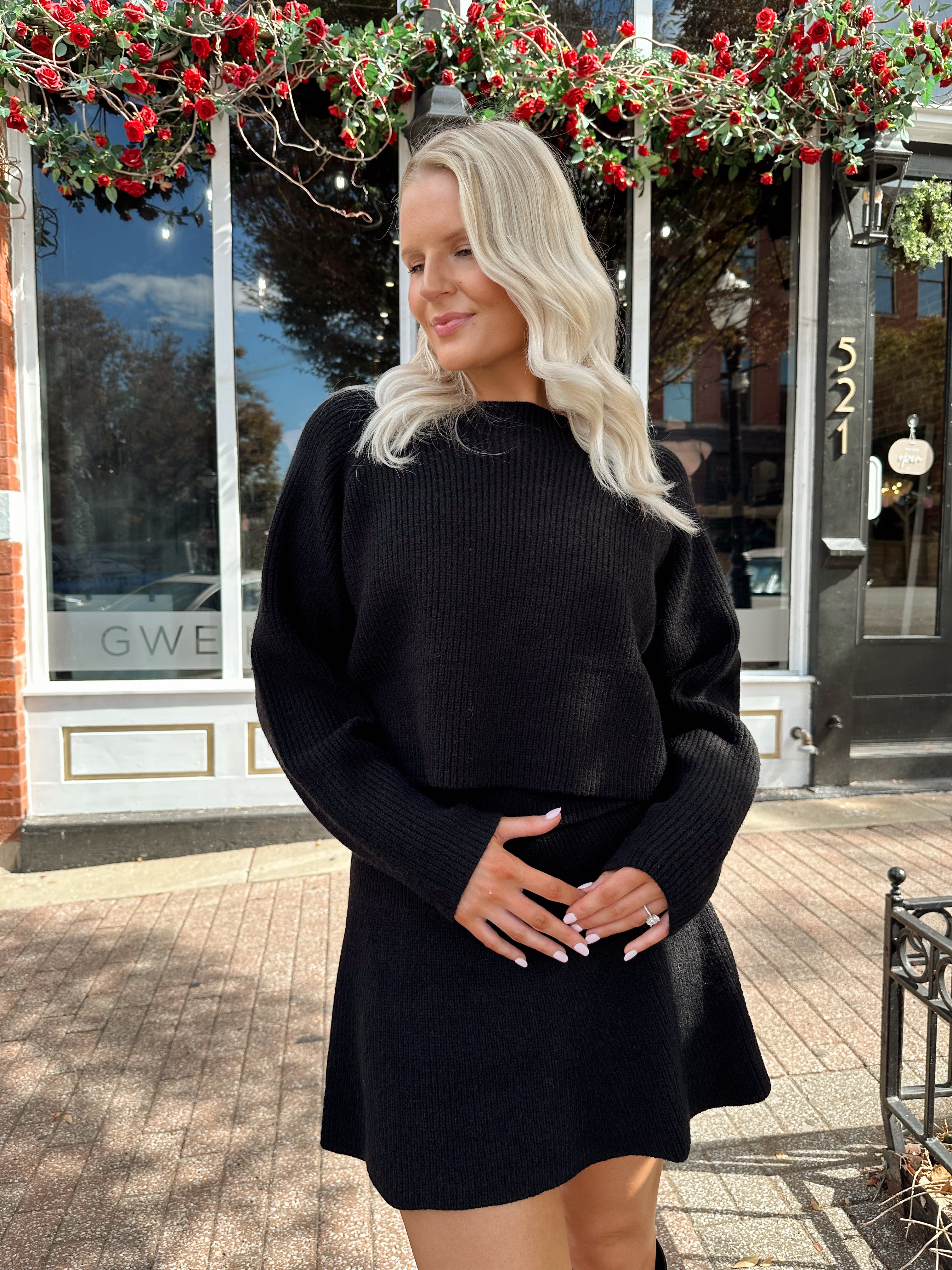 Woman wearing black sweater two piece set with long sleeve top and mini skirt. 