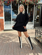 Woman wearing black sweater two piece set with long sleeve top and mini skirt. 