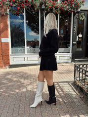 Woman wearing black sweater two piece set with long sleeve top and mini skirt. 