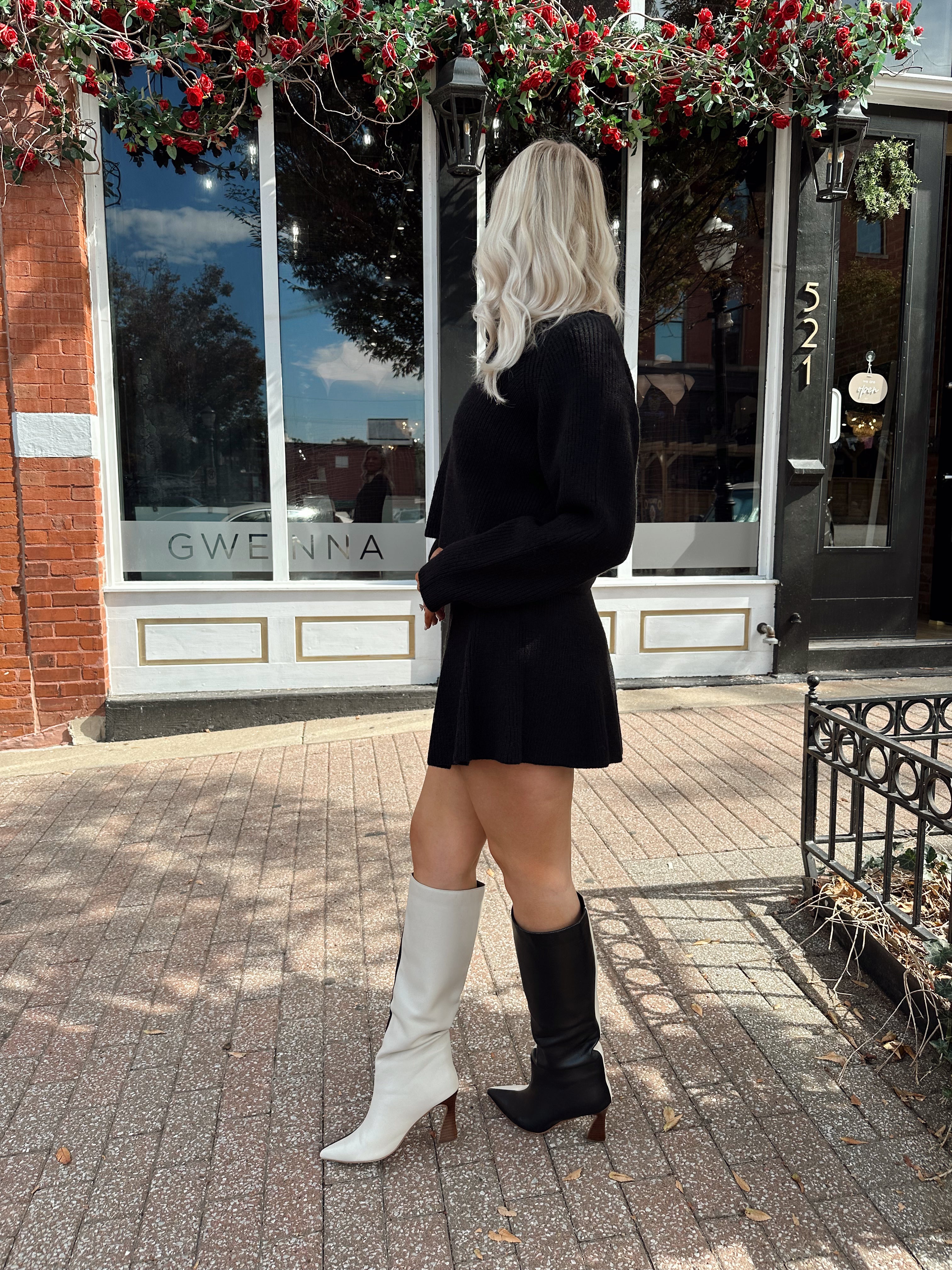 Woman wearing black sweater two piece set with long sleeve top and mini skirt. 
