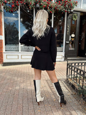 Woman wearing black sweater two piece set with long sleeve top and mini skirt. 