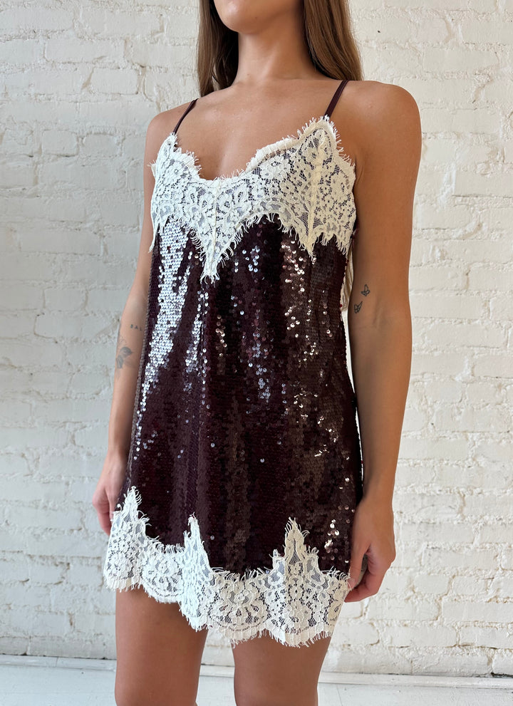 Woman wearing burgundy sequin shift mini dress with white lace trim detailing and adjustable spaghetti straps.