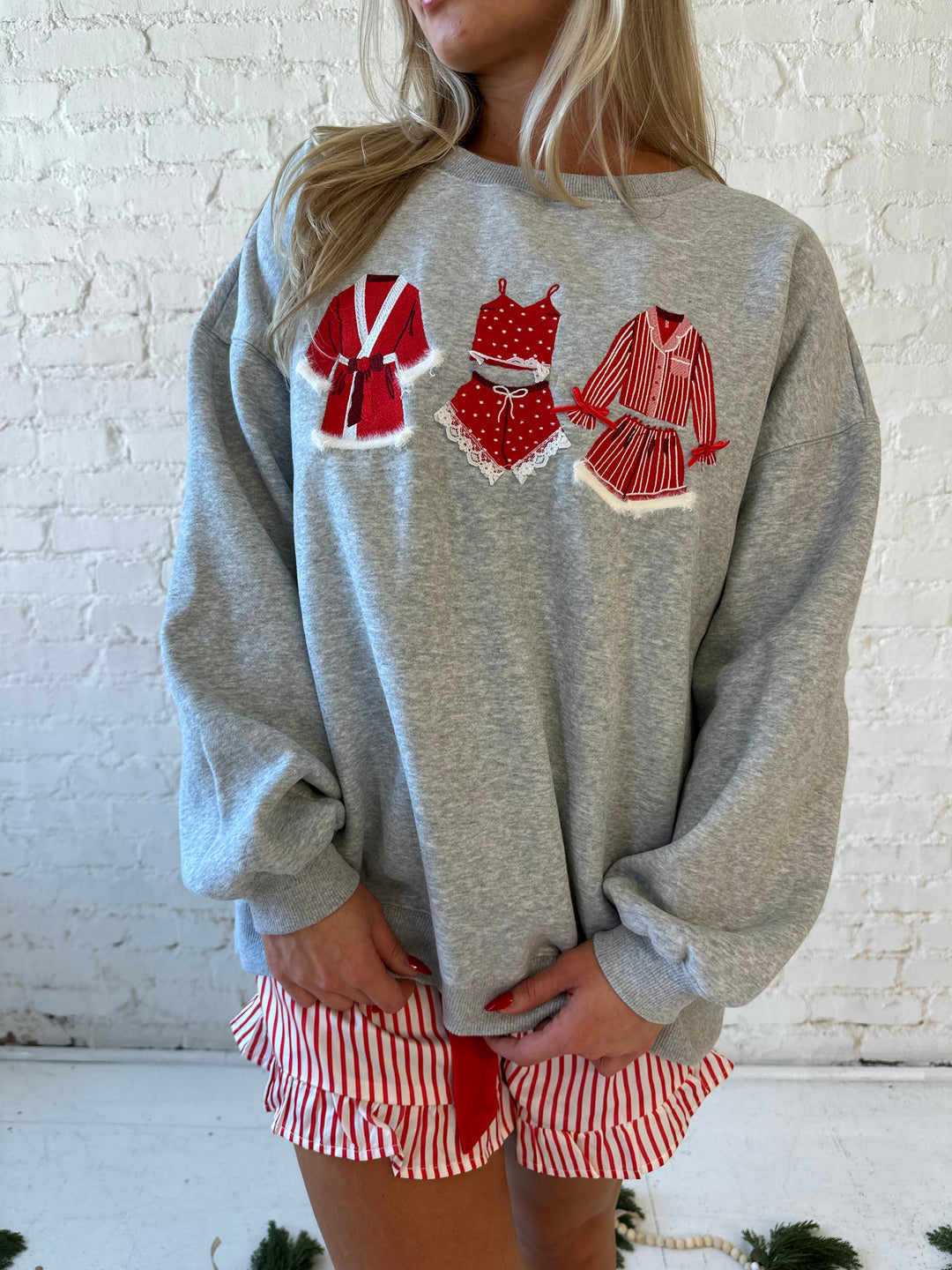 Woman wearing grey crewneck sweatshirt with red Christmas outfits embroidered on the front. 