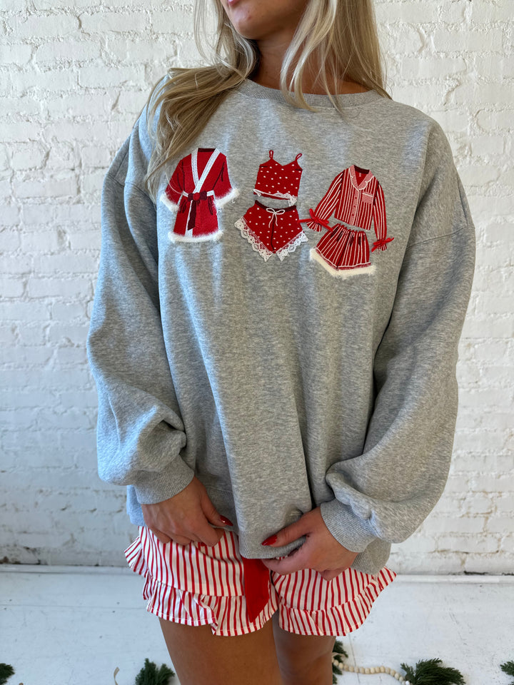 Woman wearing grey crewneck sweatshirt with red Christmas outfits embroidered on the front. 