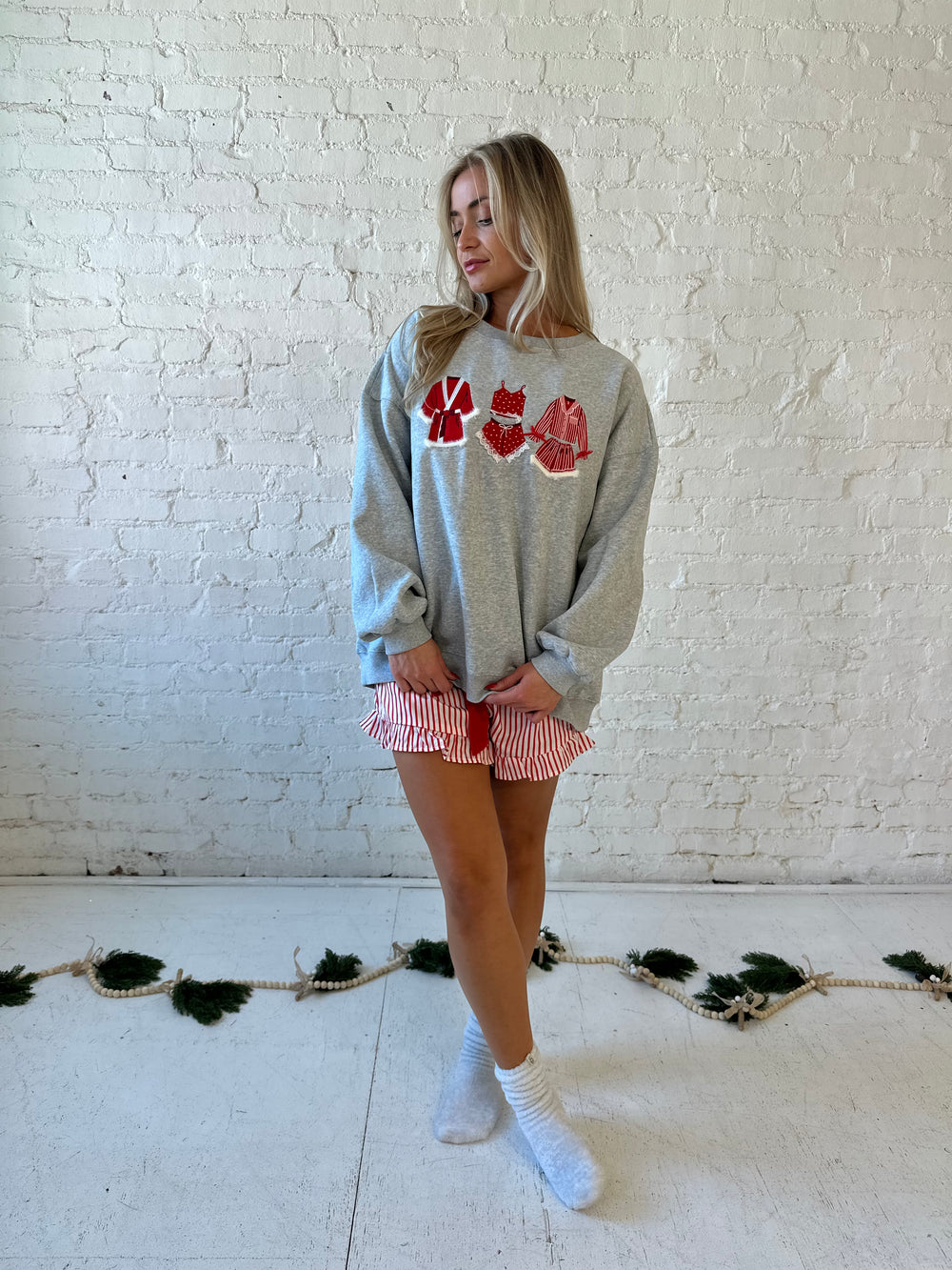 Woman wearing grey crewneck sweatshirt with red Christmas outfits embroidered on the front. 