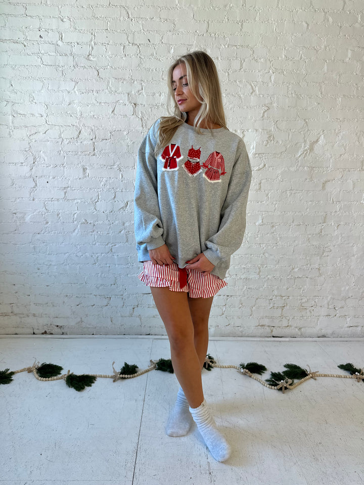 Woman wearing grey crewneck sweatshirt with red Christmas outfits embroidered on the front. 