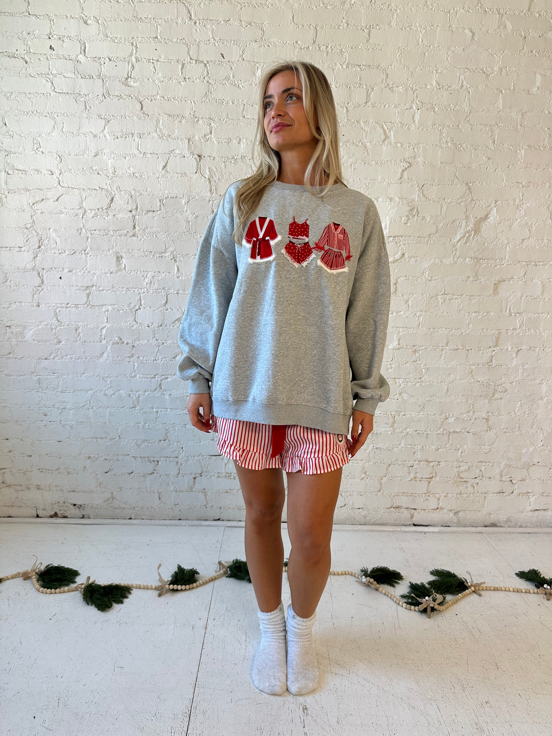 Woman wearing grey crewneck sweatshirt with red Christmas outfits embroidered on the front. 