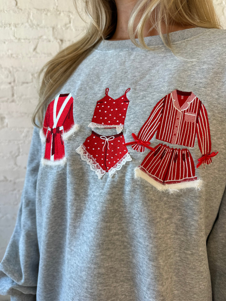 Woman wearing grey crewneck sweatshirt with red Christmas outfits embroidered on the front. 