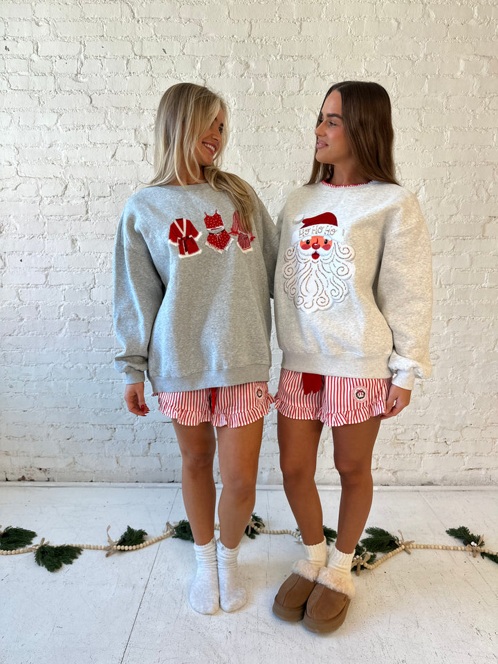 Woman wearing grey crewneck sweatshirt with red Christmas outfits embroidered on the front. 