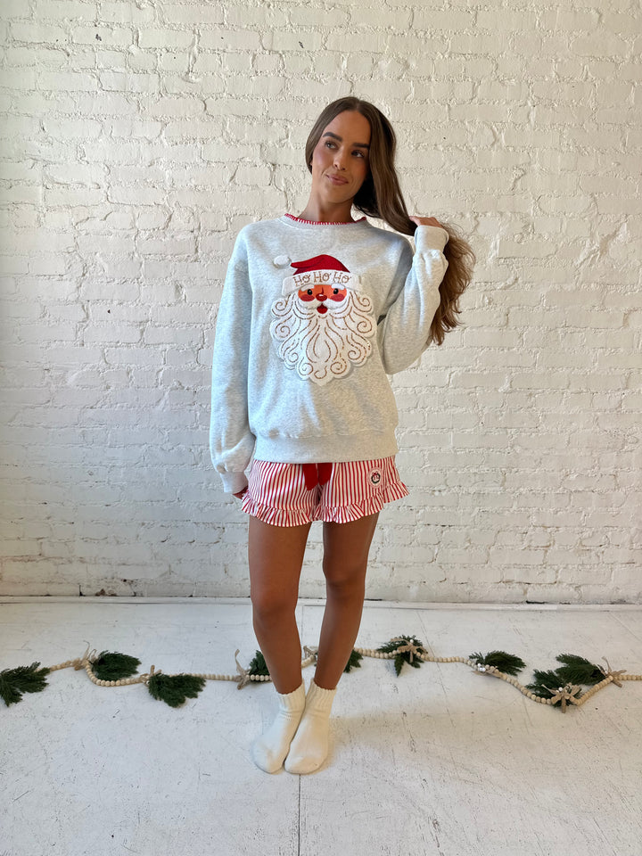 Woman wearing light grey pull over with an embroidered santa with sequin detail, and striped shorts. 