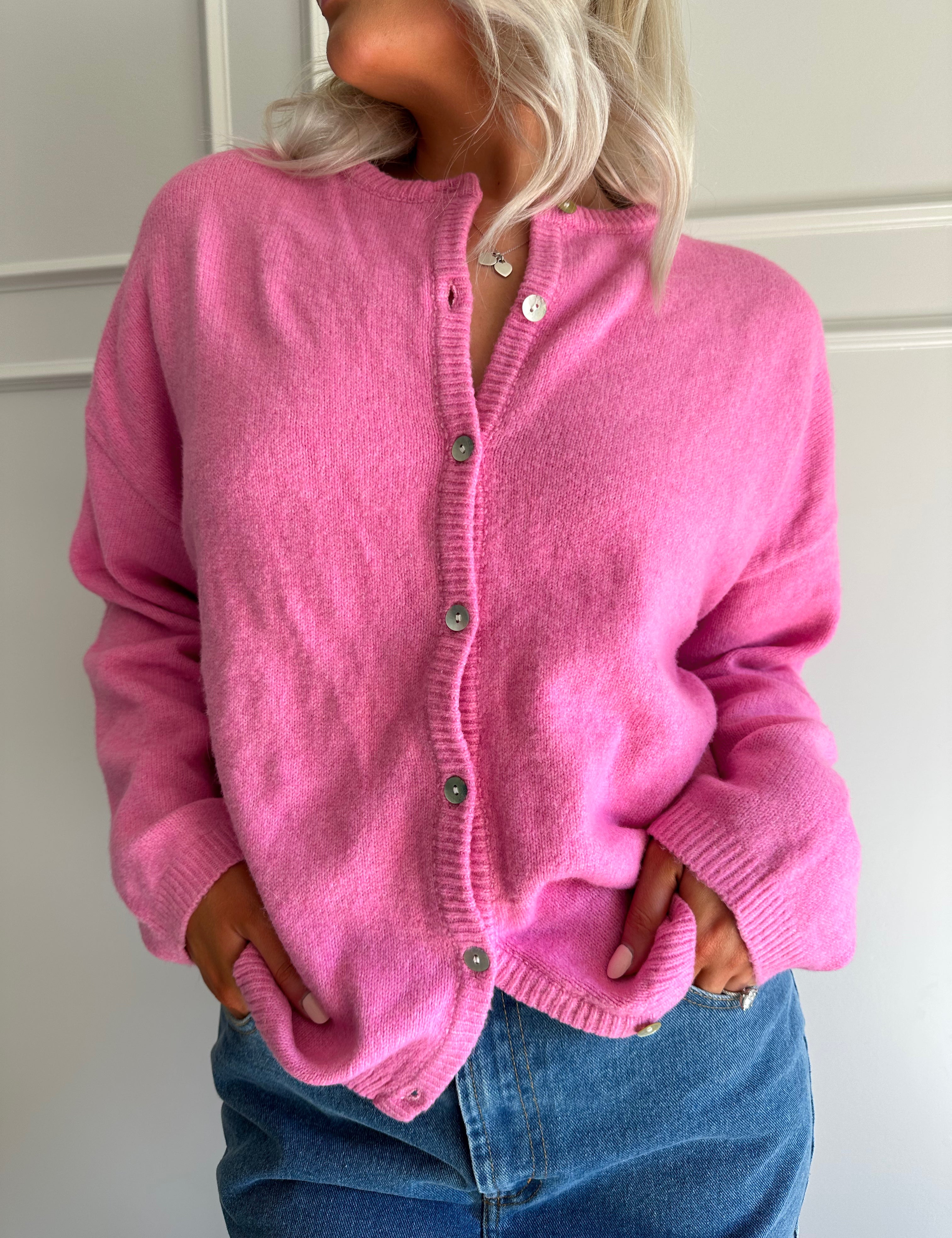 Woman wearing bubble gum pink knit button up cardigan with denim skirt. 