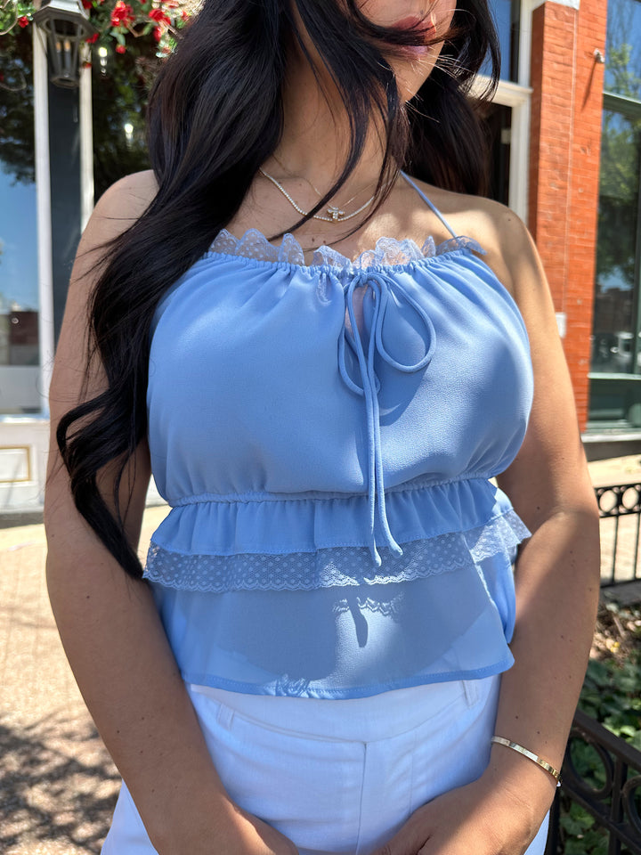 Woman wearing blue chiffon tiered halter top with open back, and white shorts
