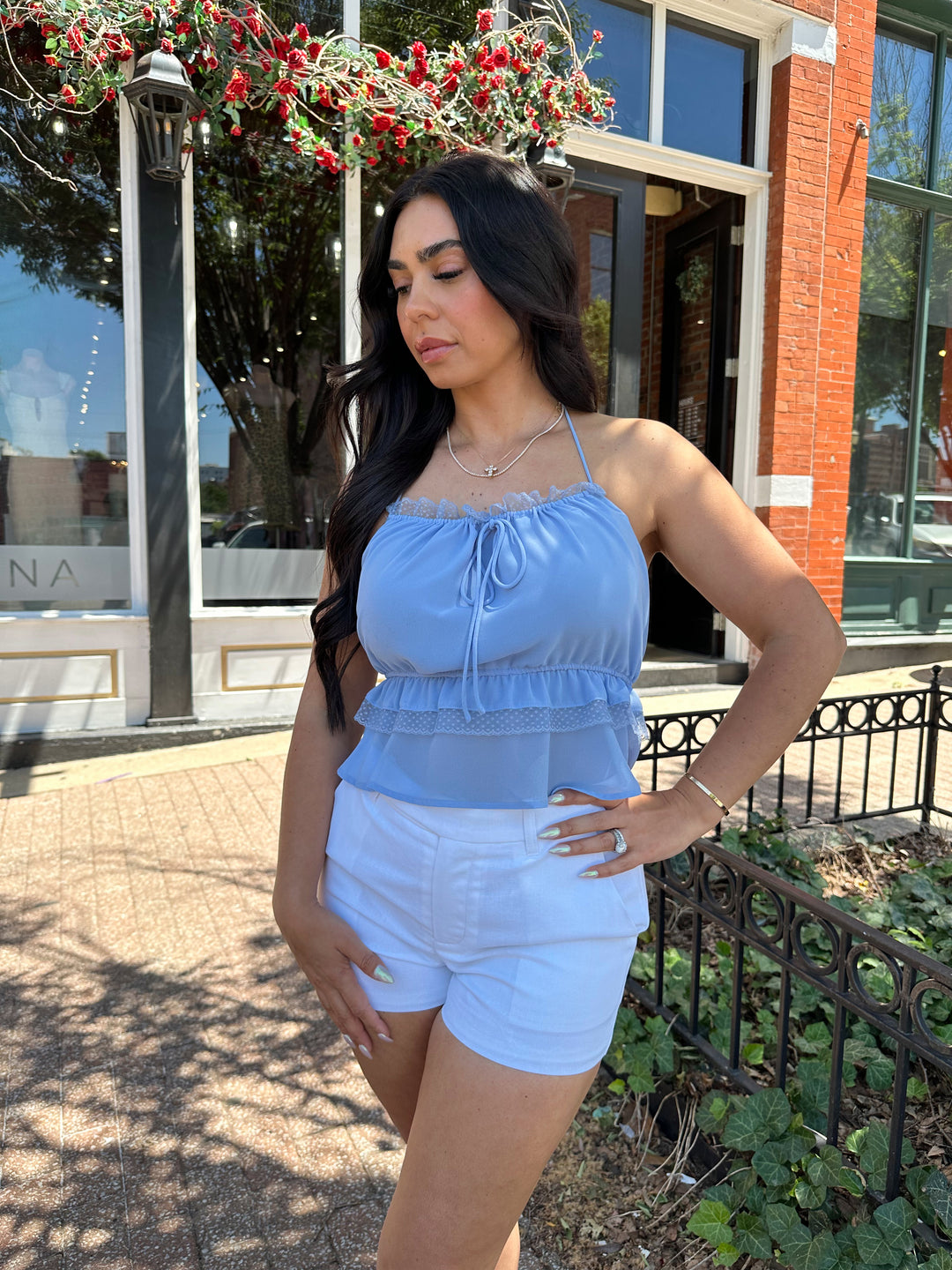 Woman wearing blue chiffon tiered halter top with open back, and white shorts
